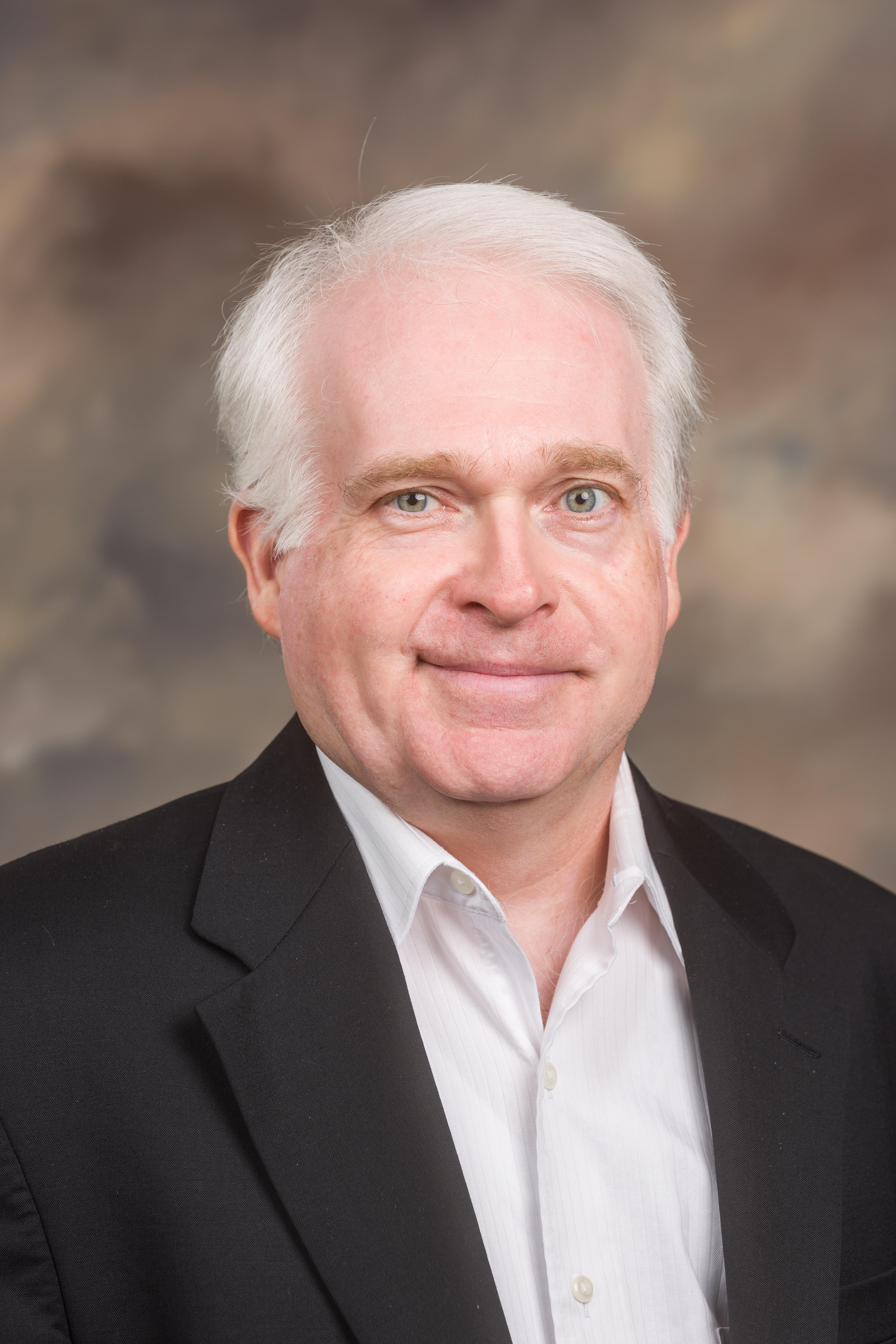 A man in a suit and tie smiles for a headshot